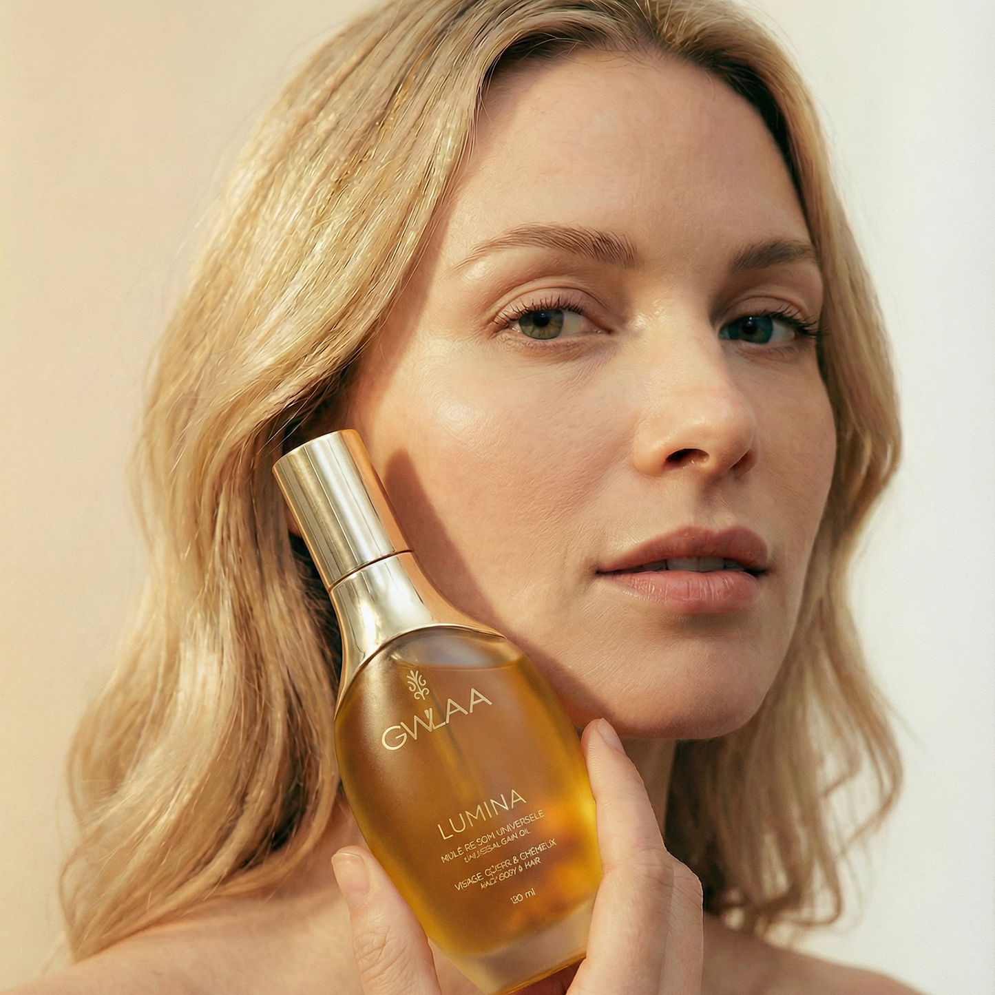 Modèle peau claire tenant le flacon Lumina de GWLAA, huile de soin universel nourrissante pour le visage, le corps et les cheveux.