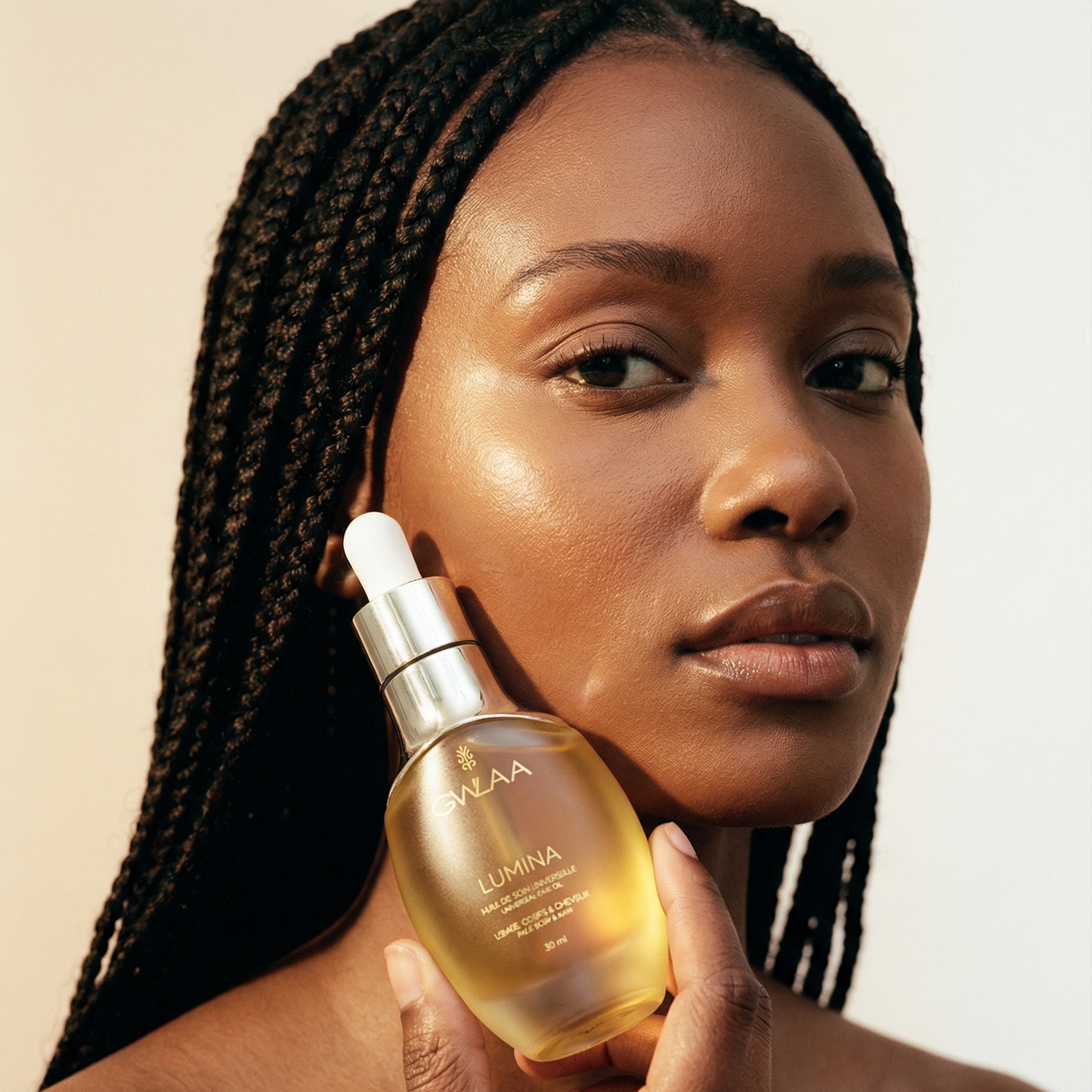 Modèle peau medium dark tenant le flacon Lumina 30ml de GWLAA, huile de soin universel nourrissante pour le visage, le corps et les cheveux.