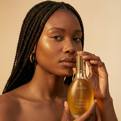 Modèle peau medium dark tenant le flacon Lumina de GWLAA, huile de soin universel nourrissante pour le visage, le corps et les cheveux.